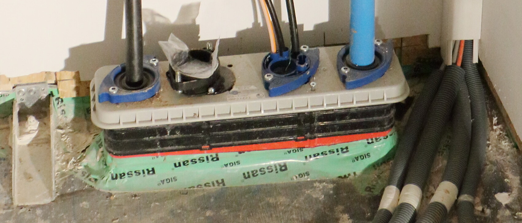 Installationsboden mit Rohranschlüssen, Kabeln und grünem Dichtband.