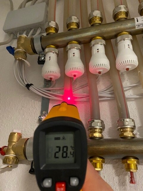 IR-Thermometer misst Temperatur an Heizungsrohr; roter Laser zeigt 28,4 °C auf Display.
