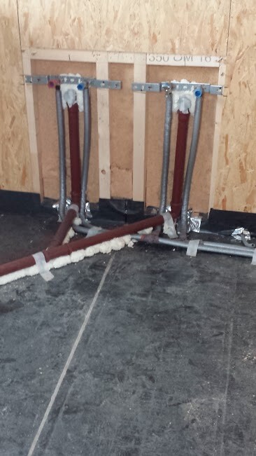 Zwei Warmwasserrohre in einer Holzständerwand, mit Dämmung und Metallhalterungen.