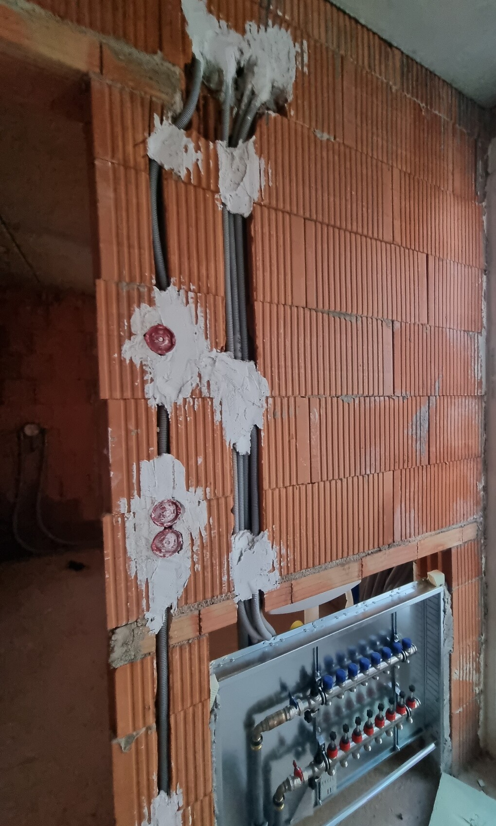 Rote Ziegelwand im Rohbau mit freiliegenden Kabelkanälen und Verteilerschrank darunter.