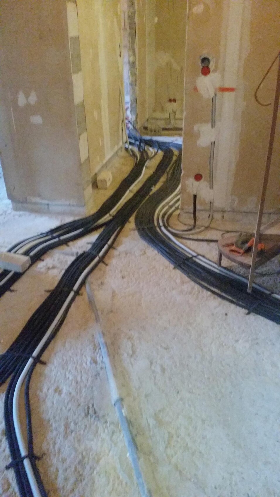 Baustelle: Mehrere schwarze Kabelbündel verlaufen über staubigen Boden zur Wand.