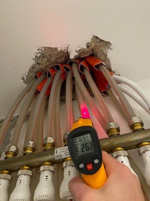 Person misst Temperatur mit IR-Laserthermometer am Kabelbündel durch ein Deckenloch.