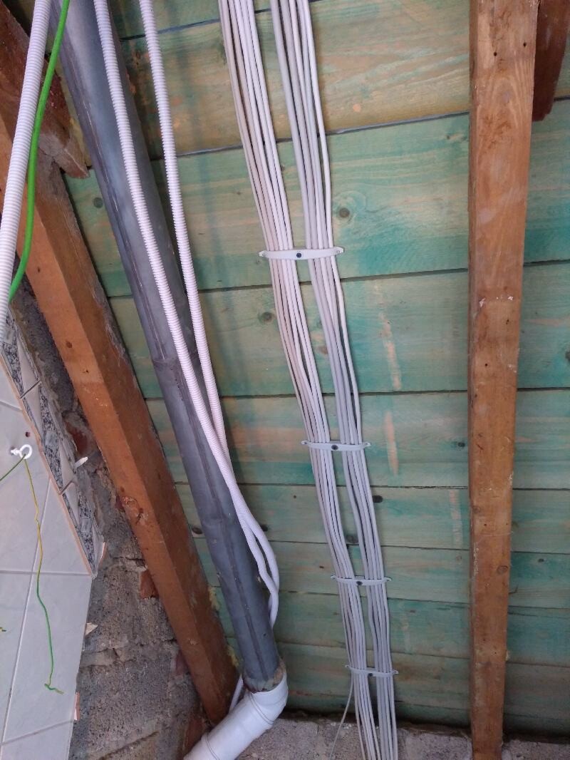 Mehrfachkabel und Rohre an einer grün gestrichenen Holzwand, mit Kabelbindern befestigt.
