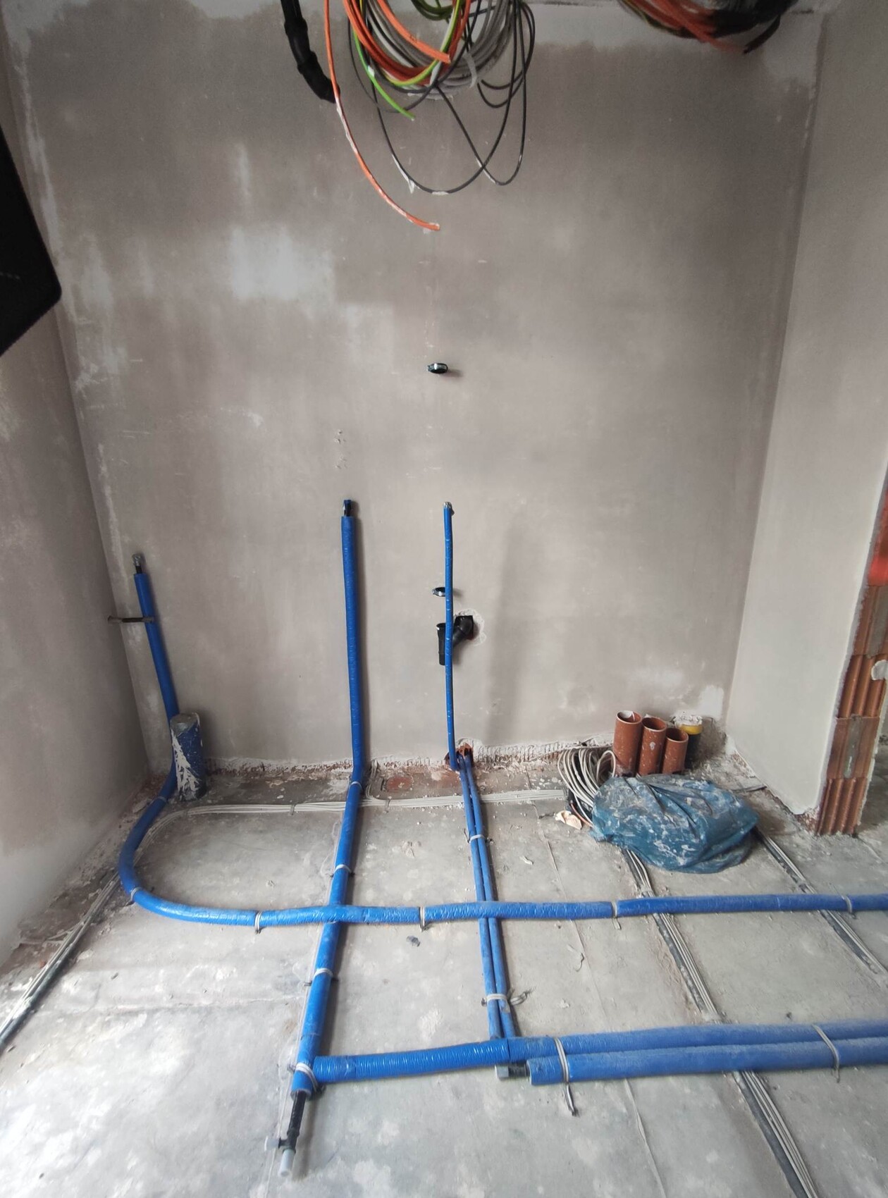 Baustellenraum: blaue Wasserrohre verlaufen am Boden, lose Kabel und unfertige Wände.