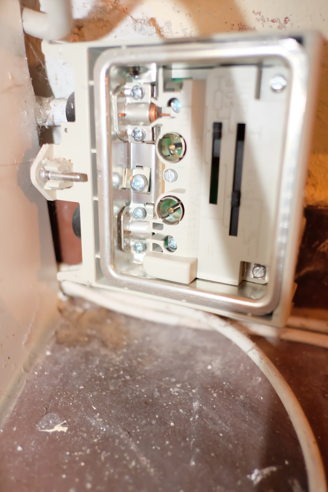 Nahaufnahme eines offenen elektrischen Verteilers in der Wand mit Schraubklemmen und Staub