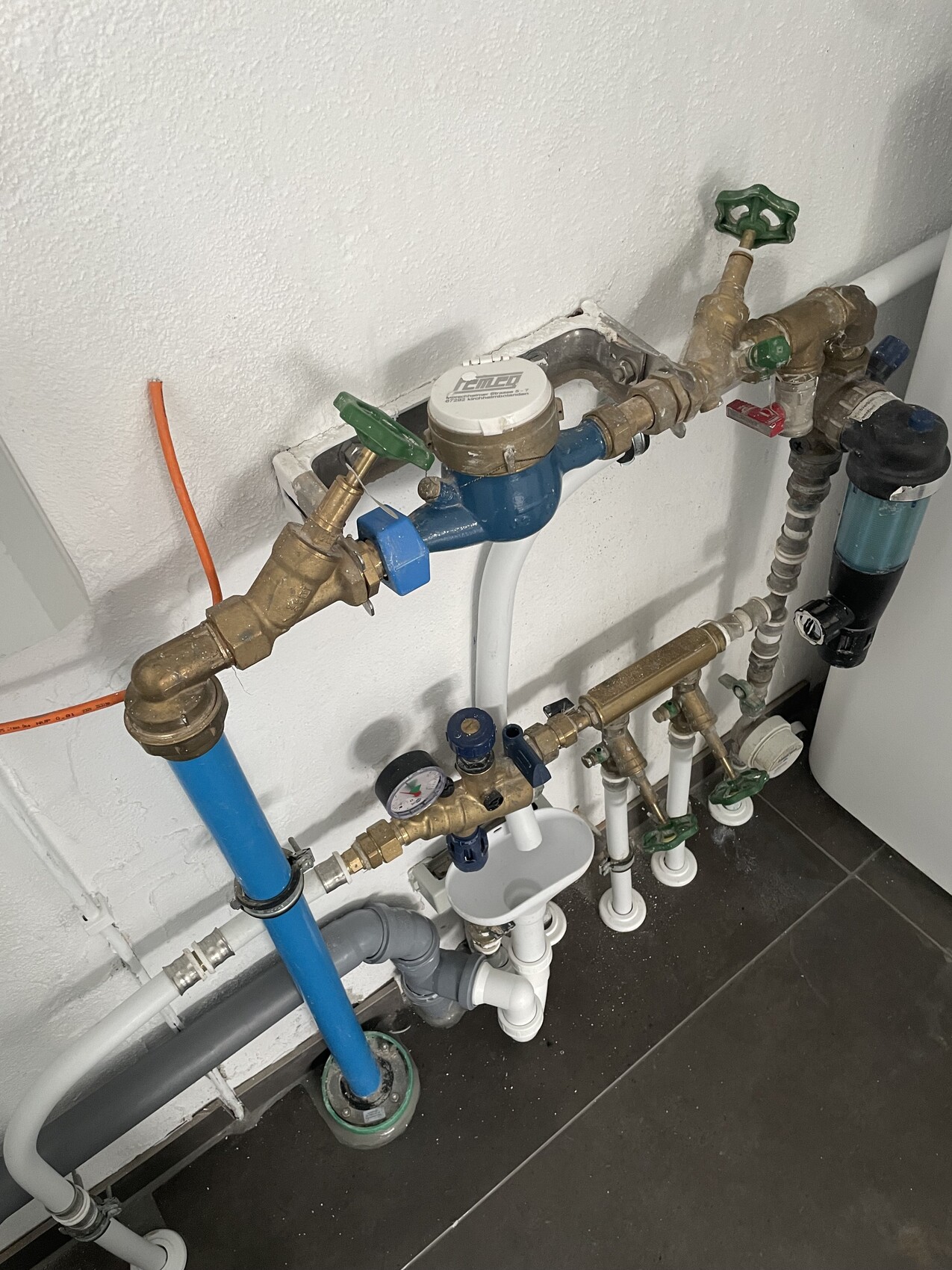 Wasserleitungen an der Wand mit Wasserzähler, Ventilen, Filter und Rohren.