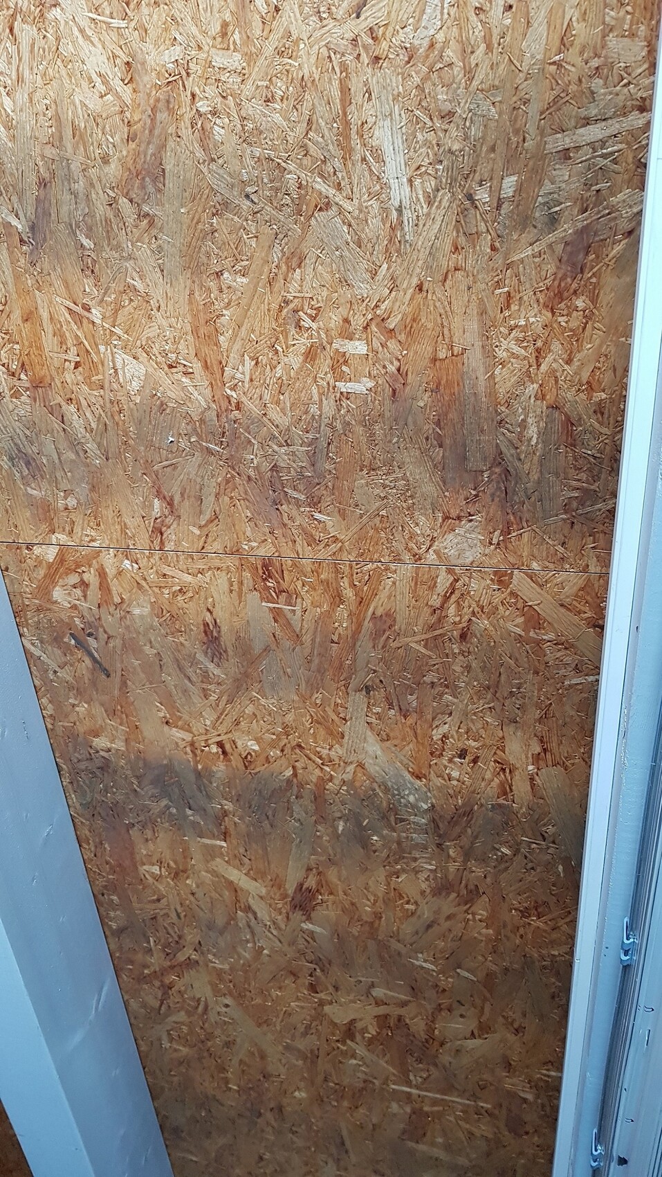 Raum mit OSB-Wandverkleidung, Türrahmen am Rand, Baustellenszene.