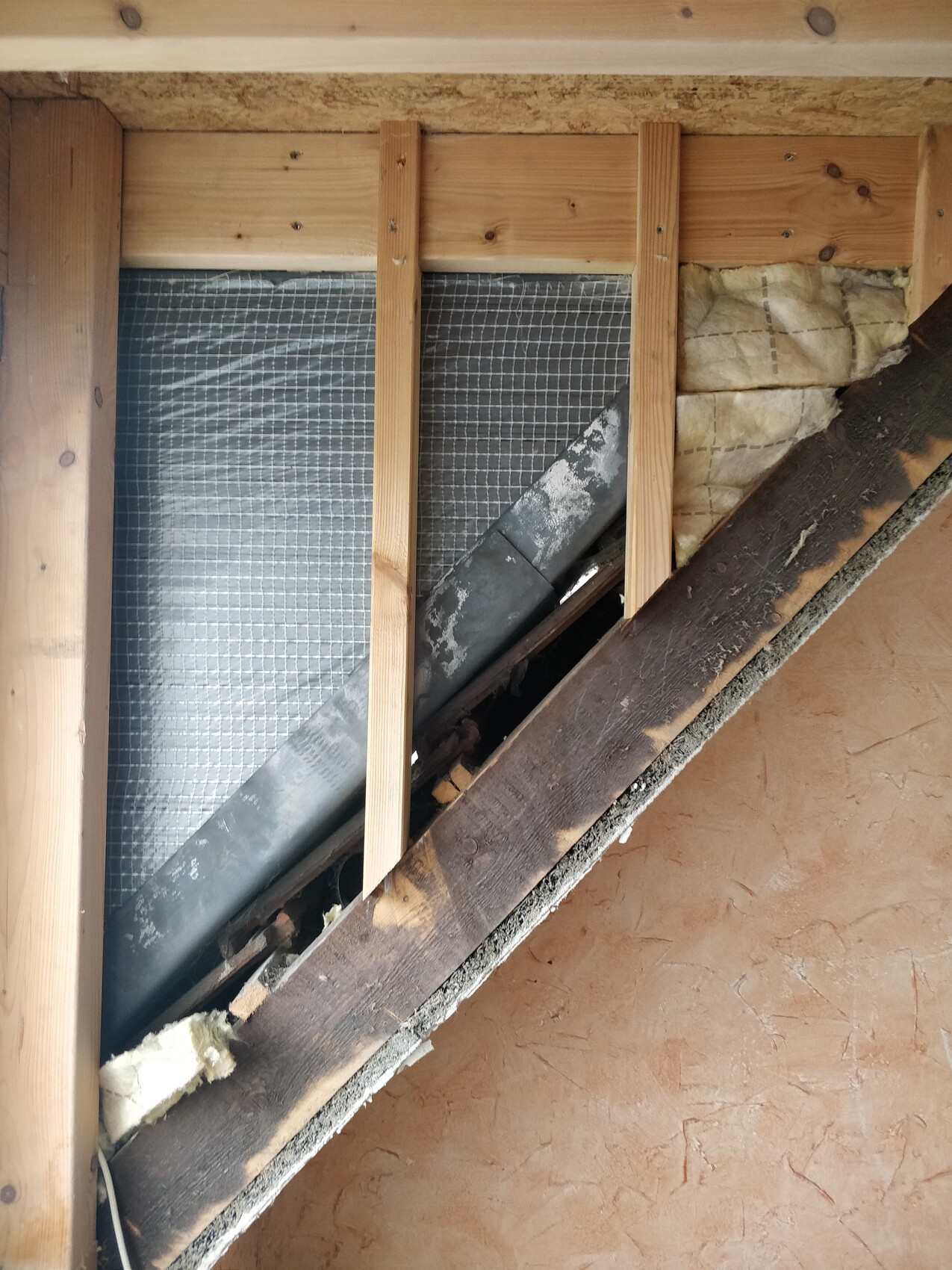 Dachboden mit Holzständern, Dämmung und einem dunklen Rohrkanal entlang der Wand.