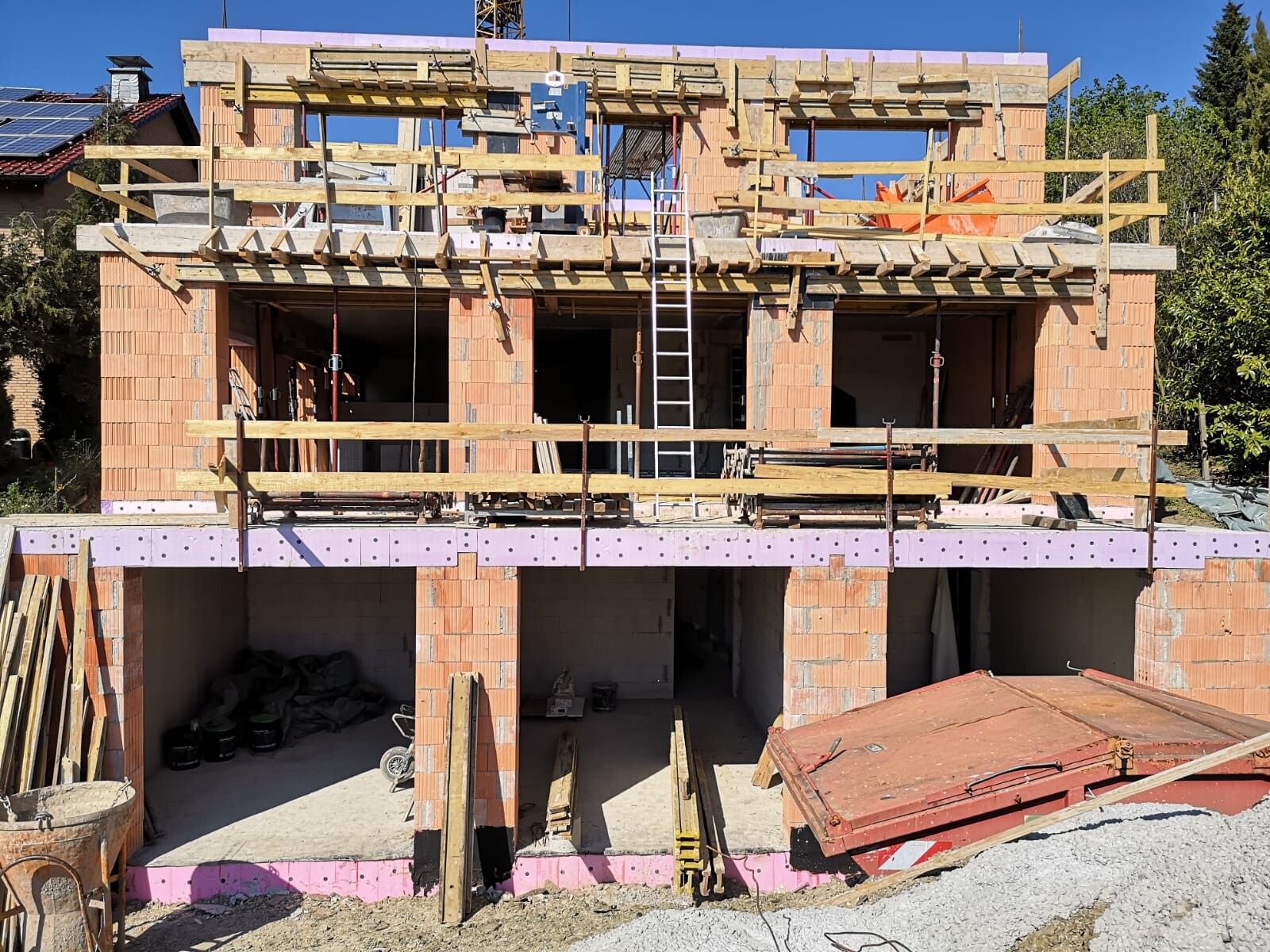 Rohbau eines zweistöckigen Ziegelhauses mit Holzgerüst, Leiter, Kran und Baumaterialien.