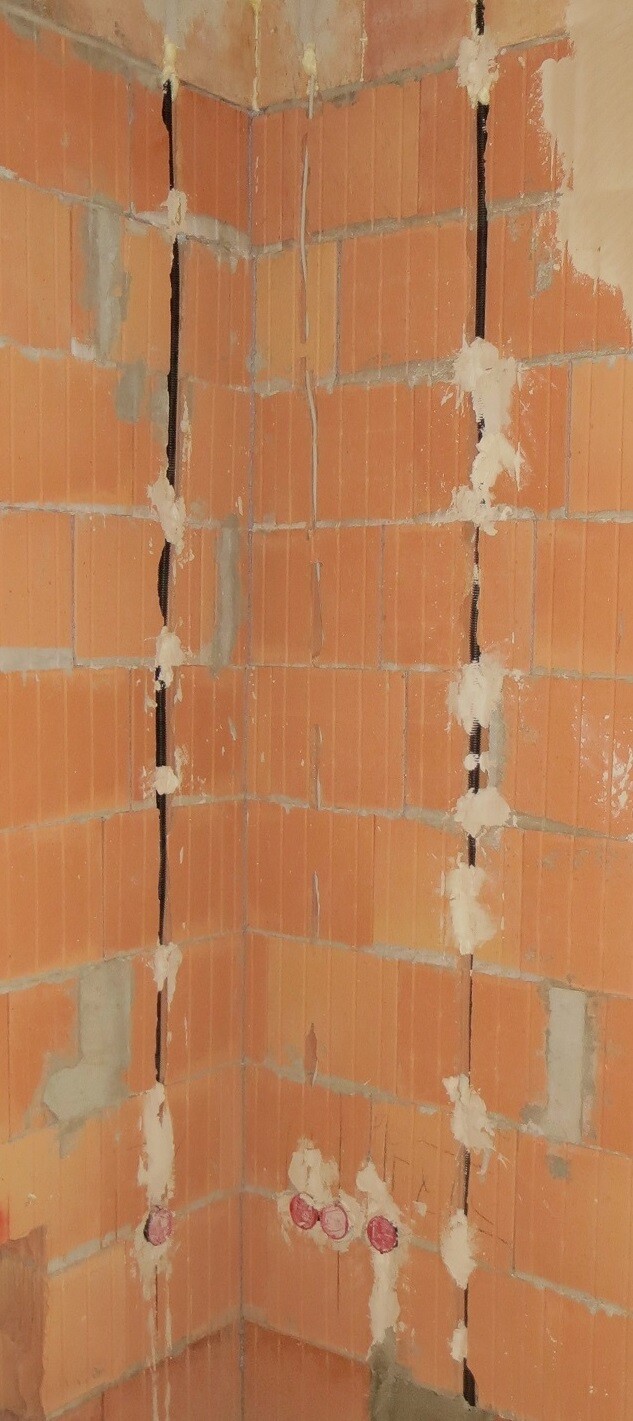 Unverputzte rote Ziegelwand in einer Innenraum-Ecke mit Rissen und Mörtelresten.