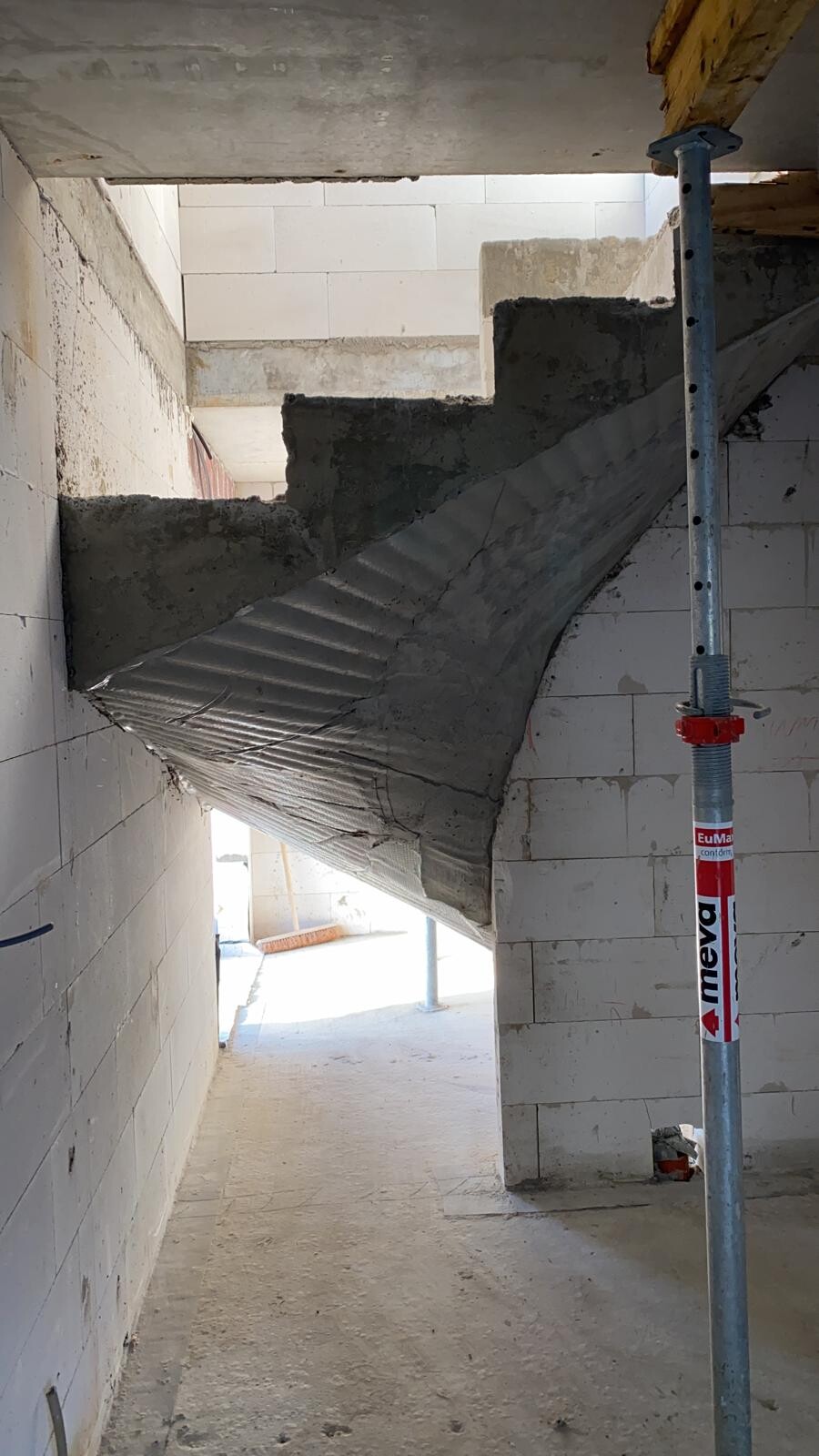 Unverputzte Betontreppe im Rohbau einer Baustelle mit Stütze.