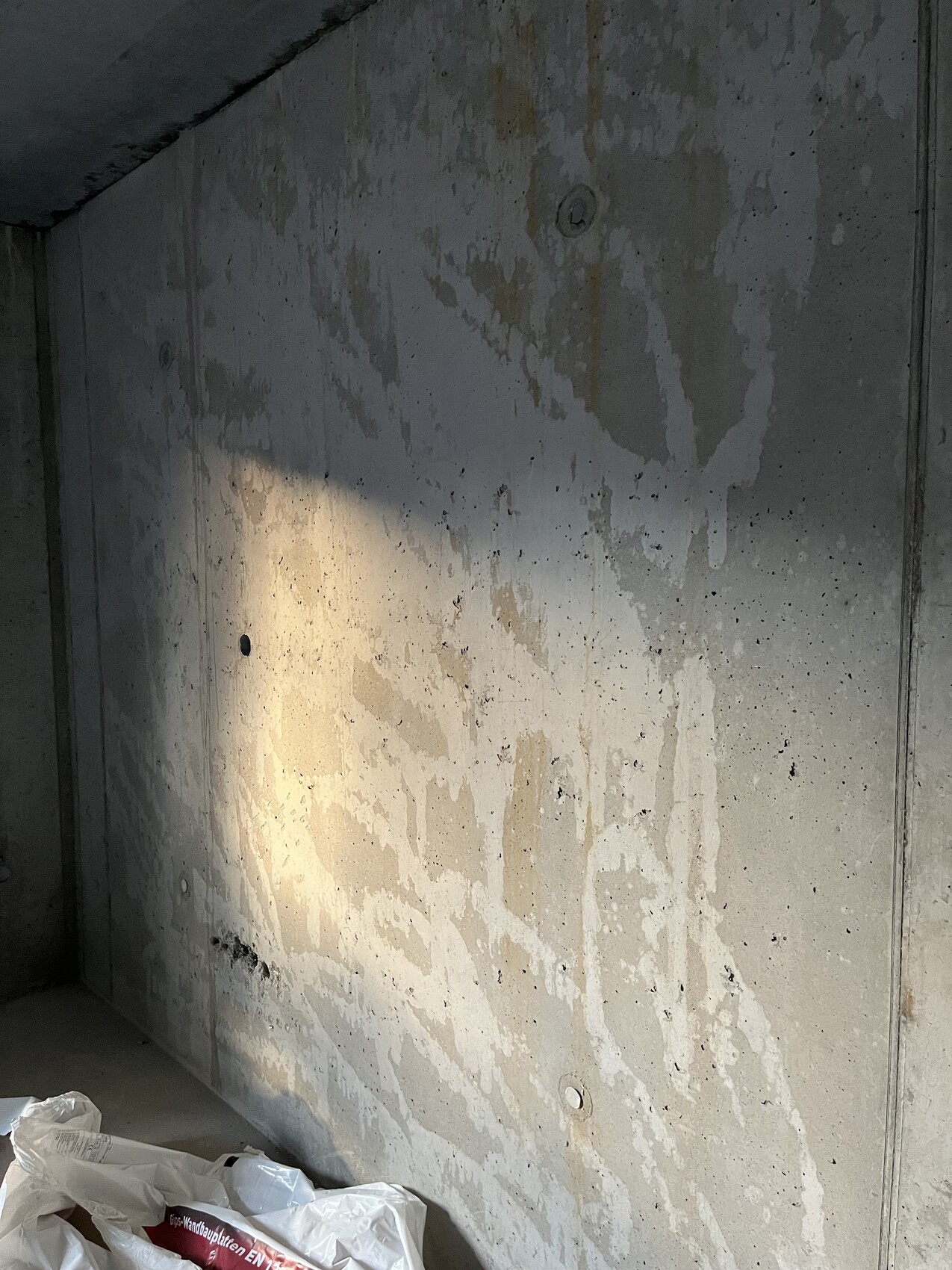 Unverputzte Betonwand im Rohbau mit Feuchtigkeitsspuren und Bauabfällen.