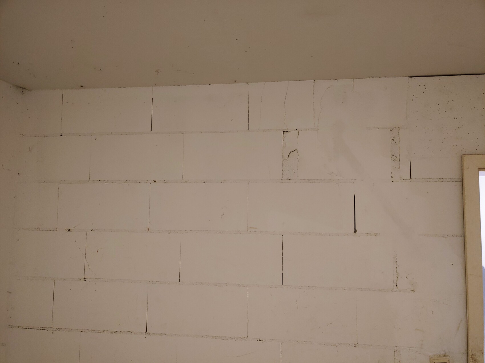Weiße Innenwand aus Betonblocksteinen, unregelmäßig verputzt, Türrahmen rechts sichtbar.