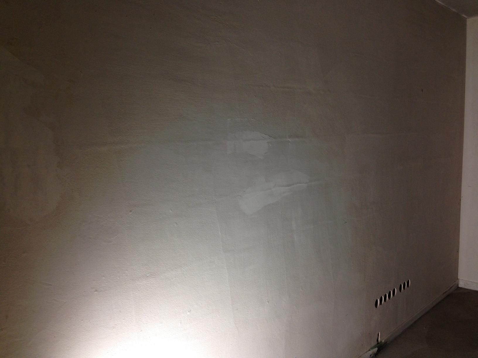 Unverputzte Innenwand im Rohbau mit unebener Oberfläche und Lüftungslöchern am Boden.