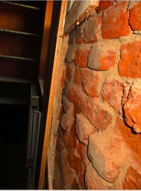 Unverputzte Steinwand im Keller neben Treppe und Heizkörper