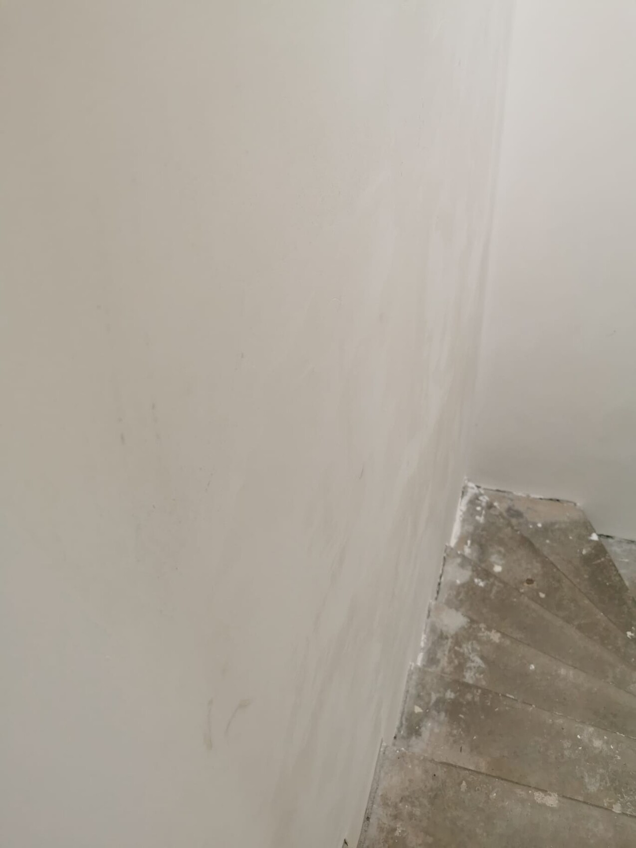 Ecke einer Treppe: weiße Wände, staubige Stufen mit Putzresten.