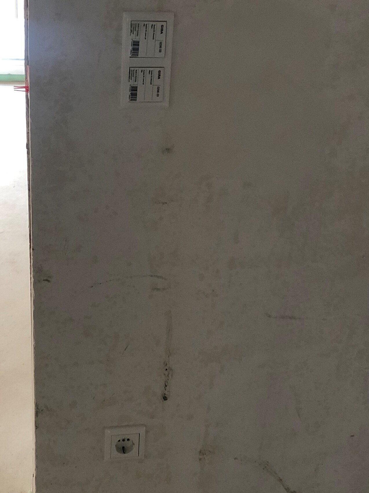 Rauhe Betonwand mit Steckdose unten links und Etikett mit Barcodes oben links