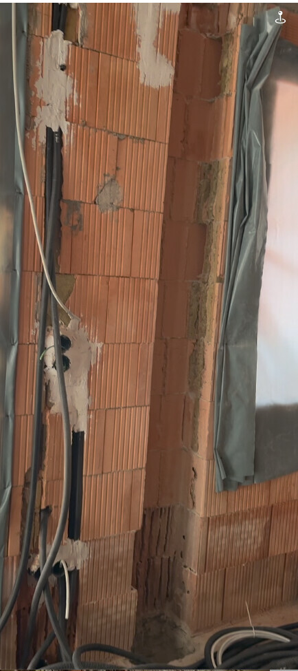 Rote Ziegelwand im Rohbau mit Kabeln, Putzresten und Plastikfolie