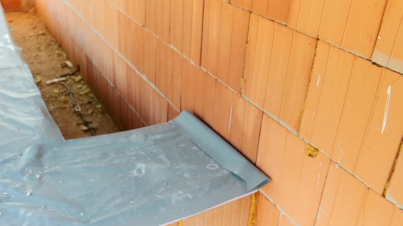 Außenansicht einer unverputzten Ziegelwand im Rohbau mit Baumaterial im Vordergrund.