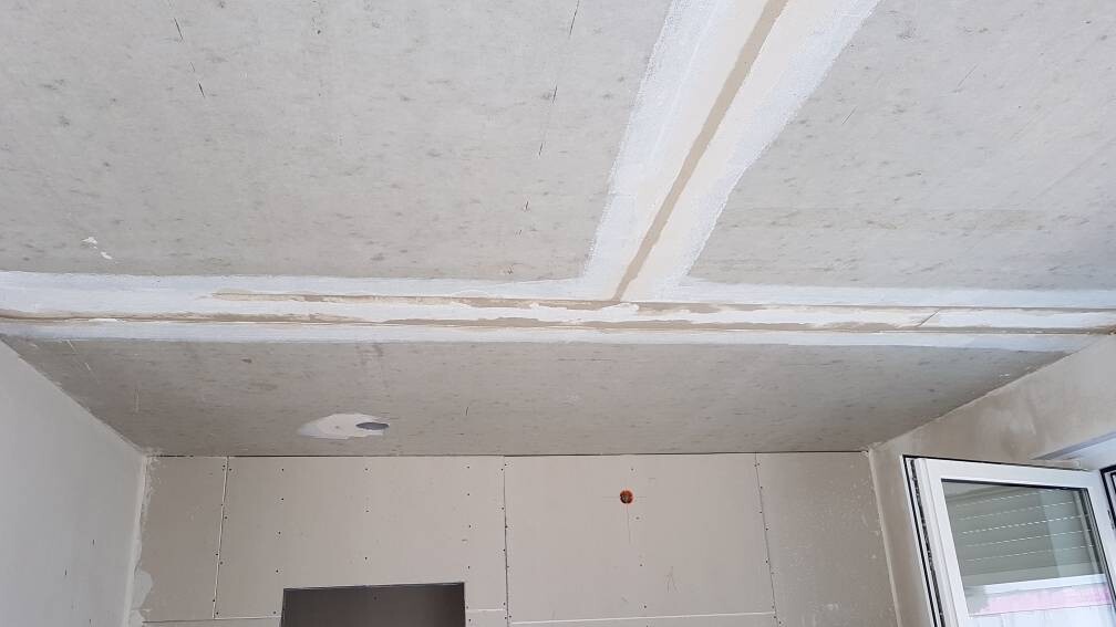 Unfertiger Bau-Raum mit Decken- und Gipskartonwänden, offenem Fenster und Loch in der Decke.