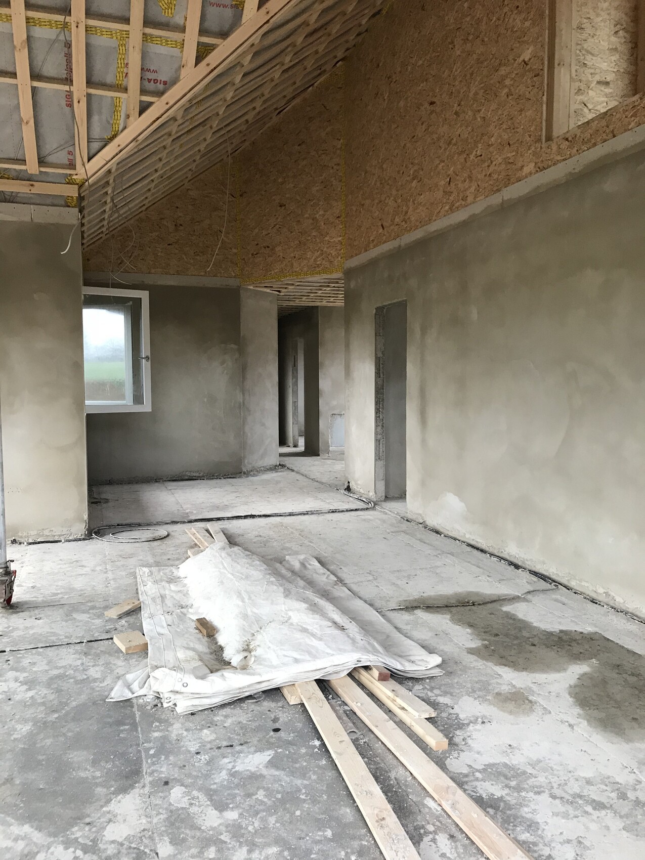 Unfertiger Innenraum einer Baustelle: rohe Wände, Holzbalken-Decke, Baumaterialien auf dem Boden.