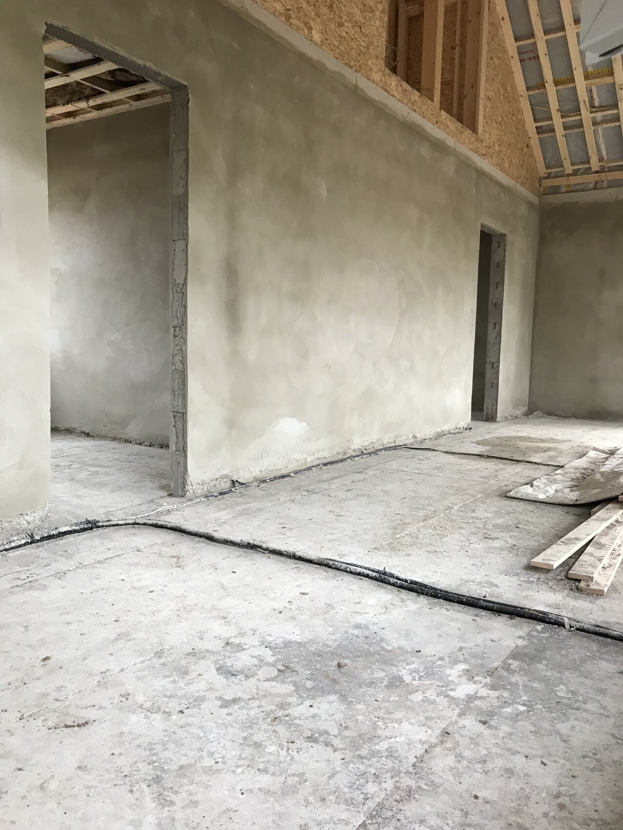 Unbearbeiteter Innenraum eines Bauprojekts mit Rohbetonwänden, Türöffnungen und Holzdecke.
