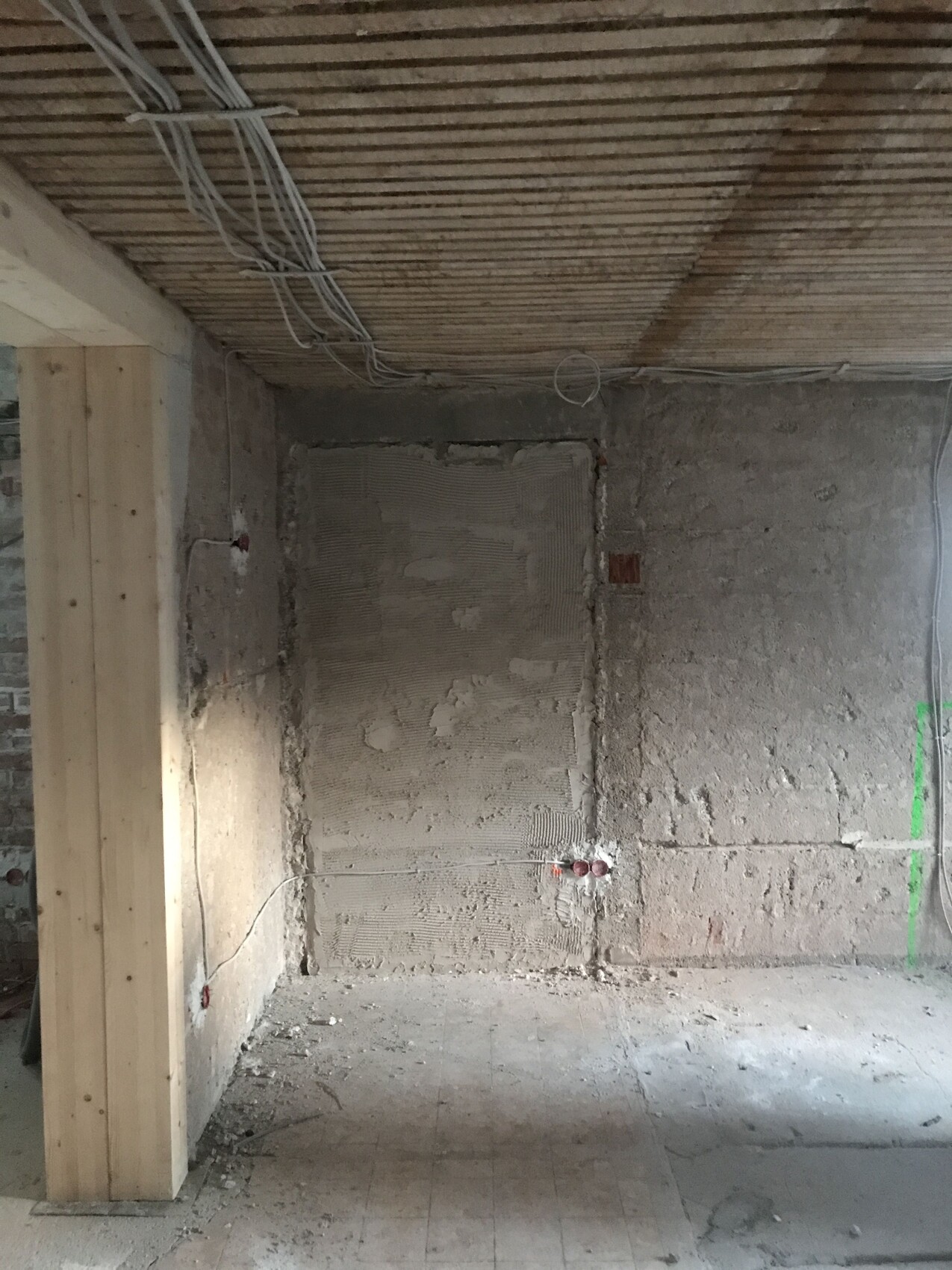 Baustelle: Raum mit rohen Betonwänden, hölzernen Deckenbalken und sichtbaren Kabeln