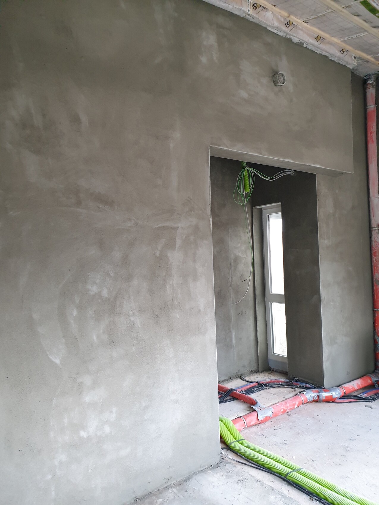 Rohbau-Innenraum: Unverputzte Betonwände, grüne Kabel von der Decke, Schläuche am Boden.