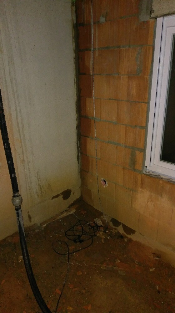 Unverputzter Kellerbereich im Rohbau mit Ziegelwand, Fenster und Kabeln.