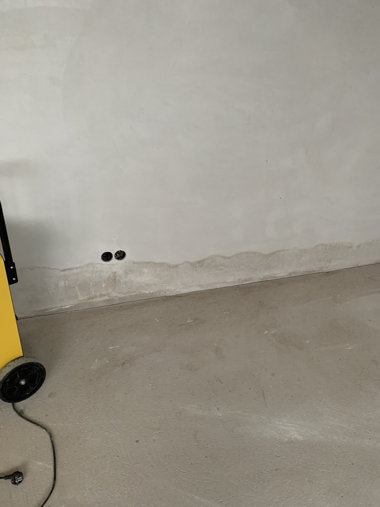 Zwei runde Wandöffnungen nahe dem Boden, gelbe Maschine mit Rädern und Kabel auf dem Boden.