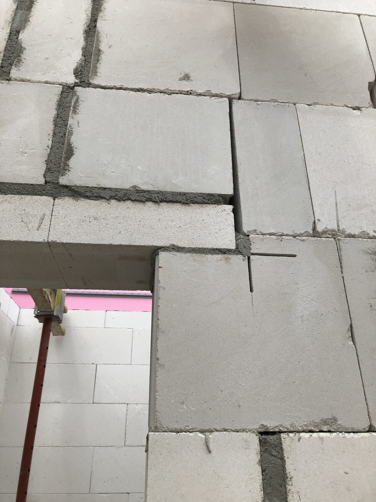 Mauer aus grauen Betonblöcken mit sichtbaren Fugen; rotes Gerüstteil im Vordergrund.