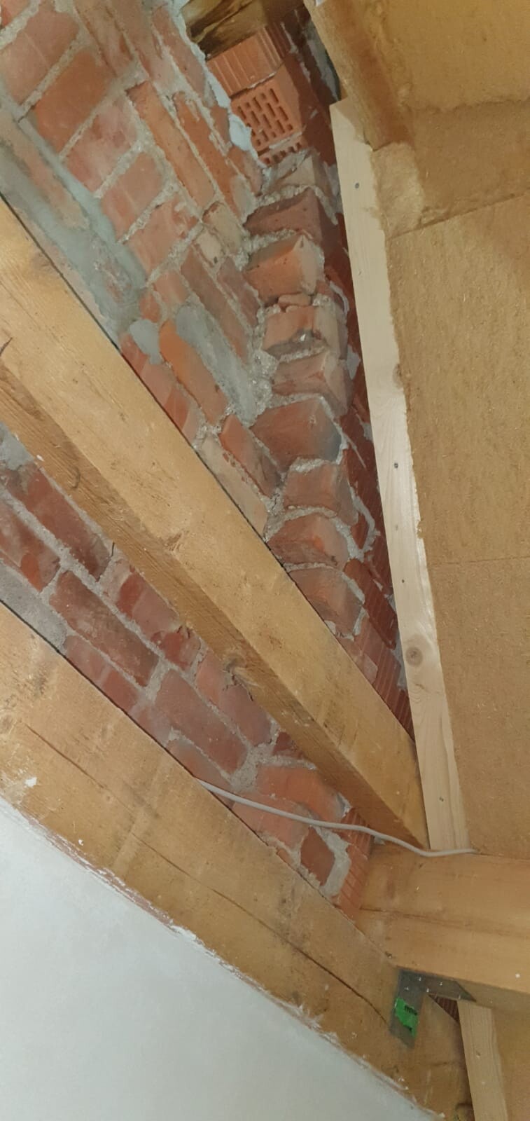 Unverputzte Backsteinwand zwischen Holzbalken; Mörtelreste sichtbar.