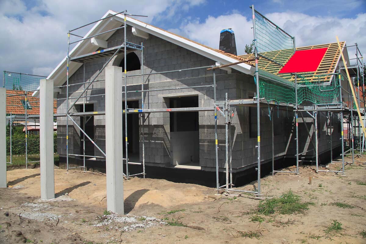 Rohbau eines Einfamilienhauses mit Gerüst, Betonblockmauerwerk und Dacharbeiten.