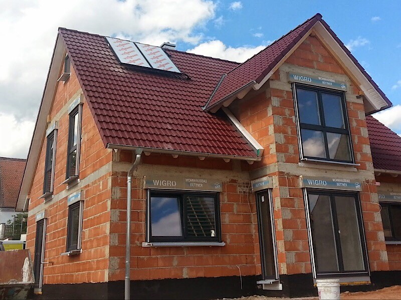 Unter Bau befindliches zweigeschossiges Ziegelhaus mit rotem Dach und Solarmodulen.