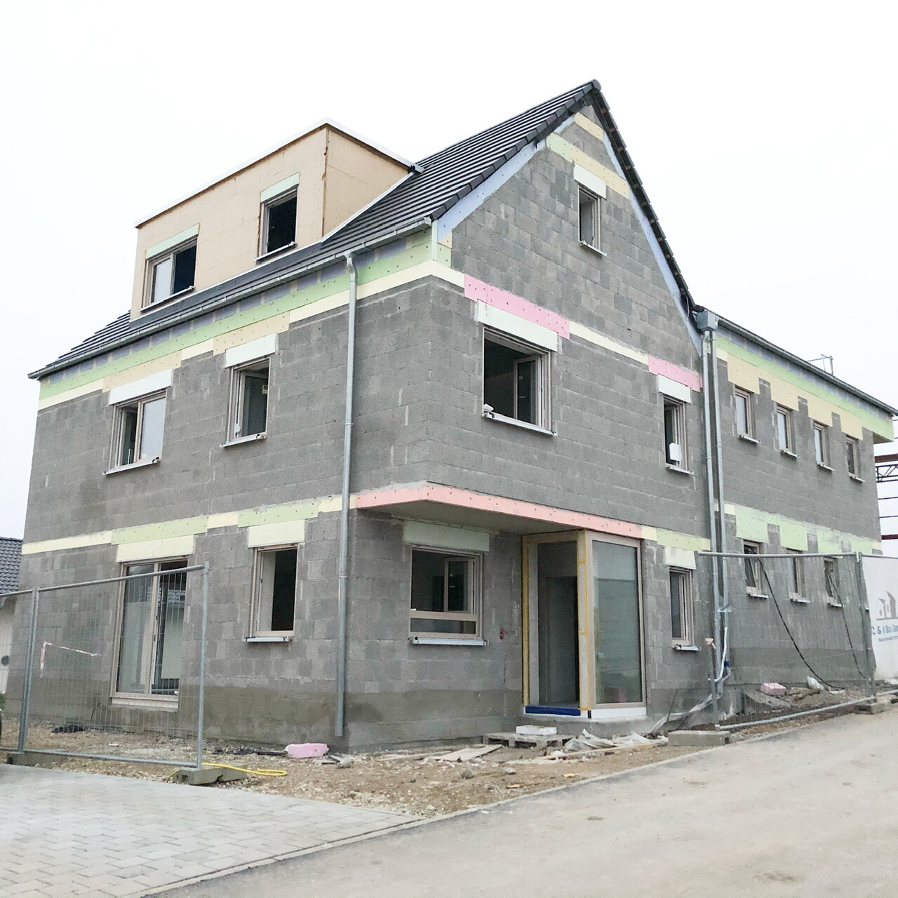 Mehrgeschossiges Rohbauhaus aus Beton mit Pastell-Dämmstreifen und Bauzaun