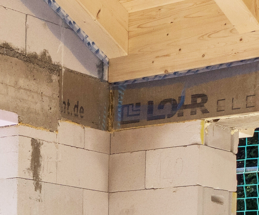 Baustellenaufnahme: weiße Betonblöcke, Holzbalkendecke und blaues Klebeband.