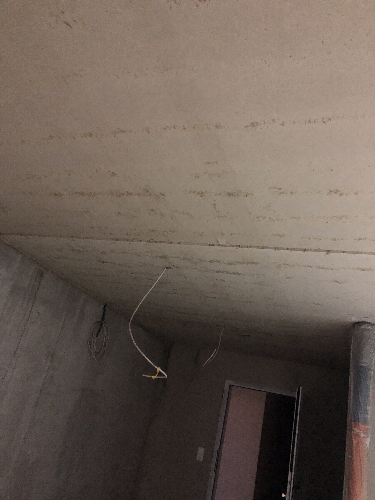Unfertiger Kellerraum mit Rohbetonwänden; lose Kabel hängen von der Decke herab.