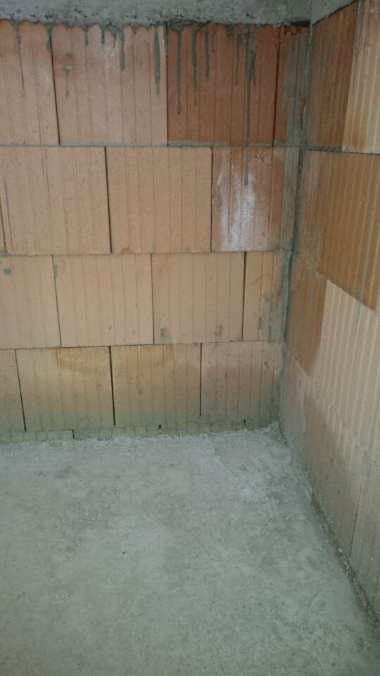 Unverputzte Kellerwand aus Ziegelsteinen mit Feuchtigkeit am oberen Rand und Betonboden.