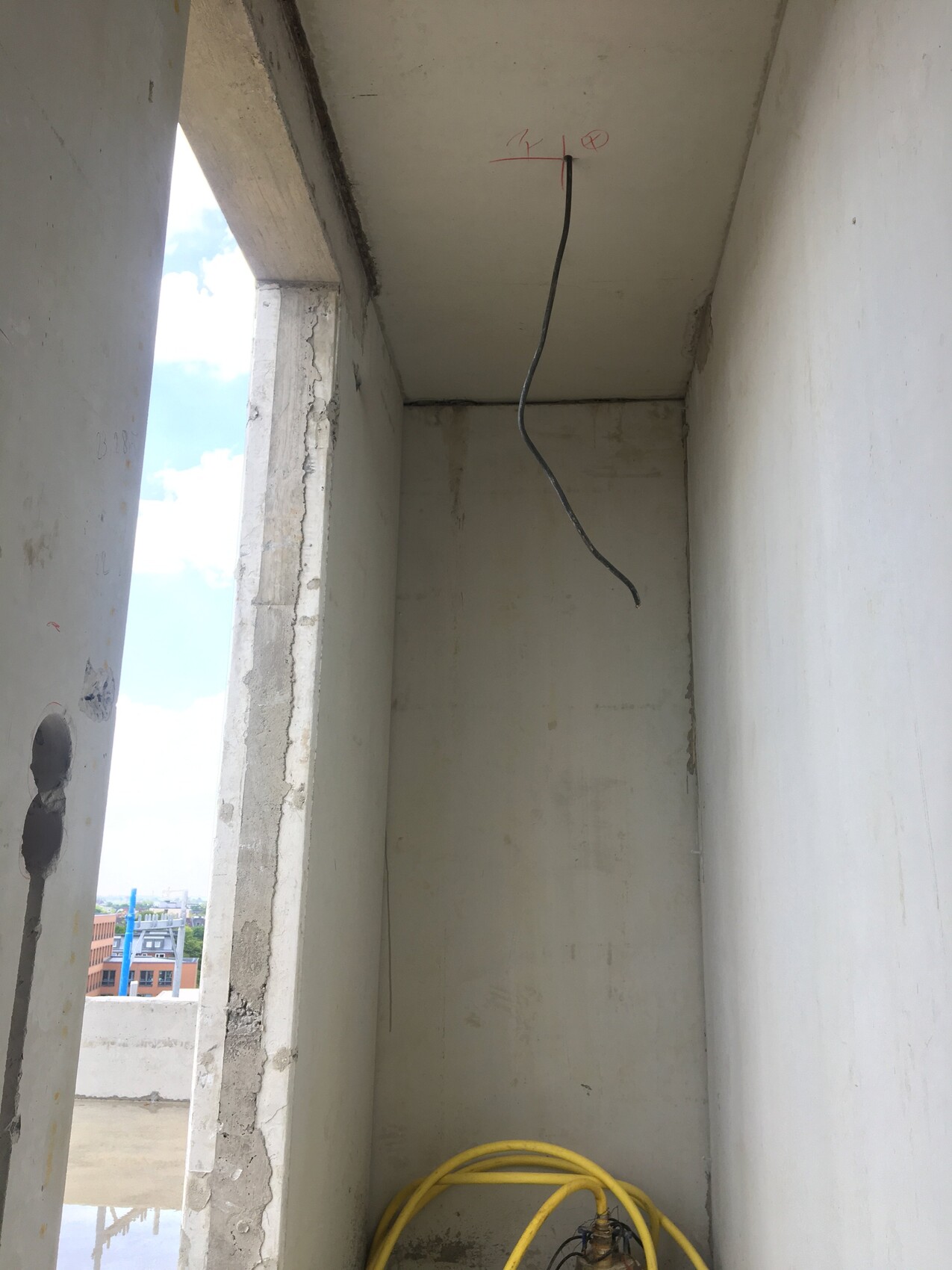 Baustellenkorridor: freiliegendes Kabel aus Decke, gelber Schlauch am Boden, Außenbereich sichtbar.