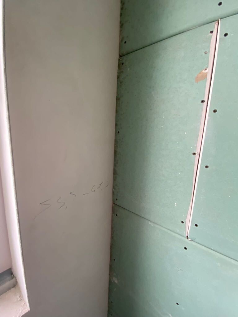 Innenraum: graue Wand neben grünen Trockenbauplatten mit Schrauben und Nahtband an der Stoßstelle.