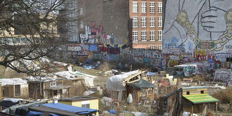 Blick auf eine urbane Siedlung mit provisorischen Hütten und graffiti-bemalten Mauern.