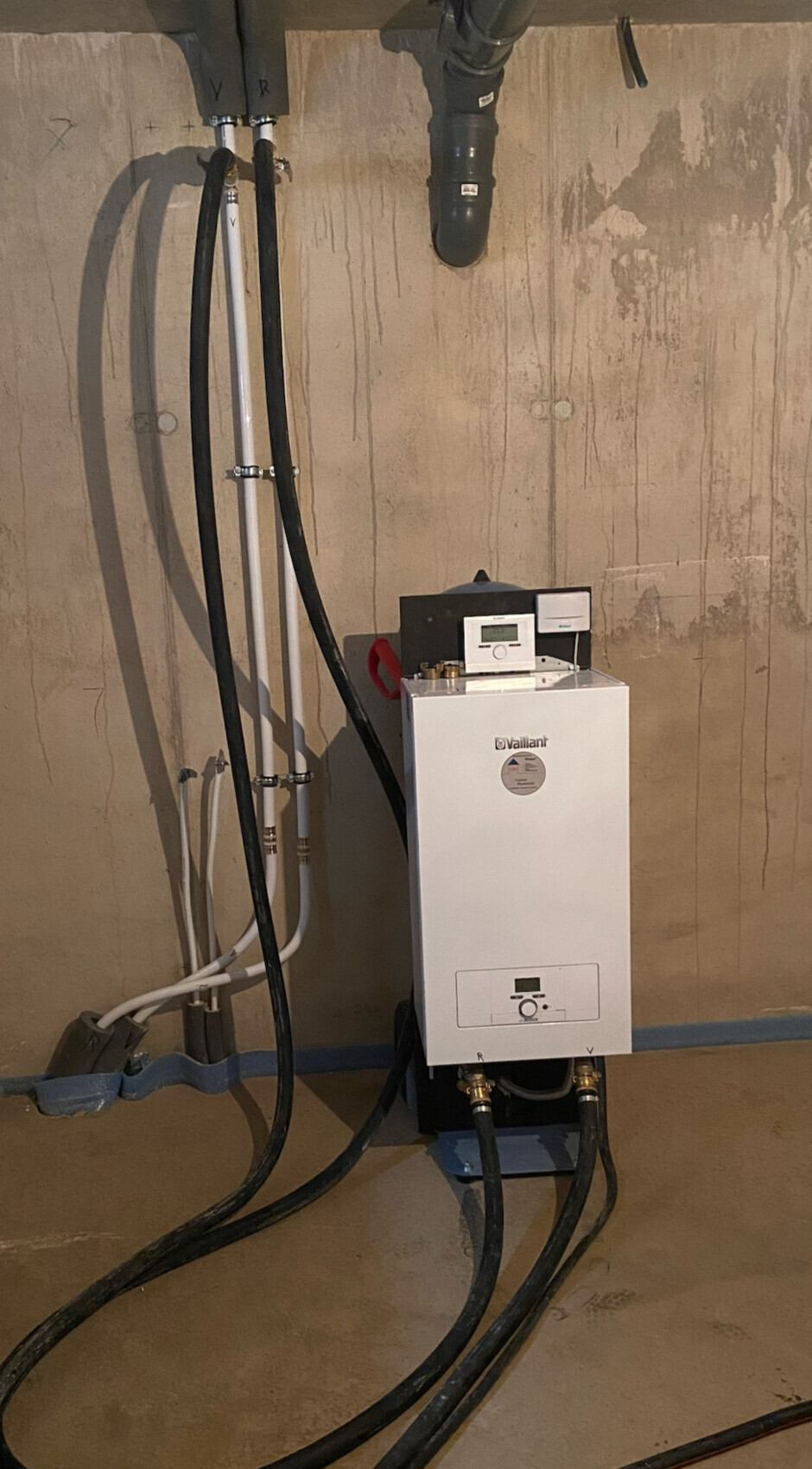Vaillant Gasbrennwertkessel im Keller, umgeben von schwarzen Schläuchen und Rohrleitungen.