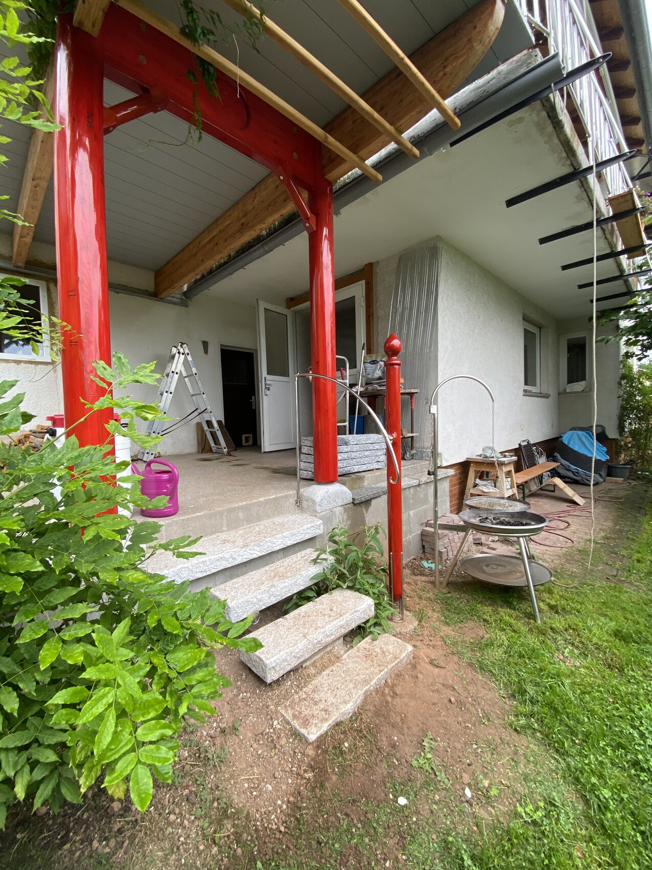 Veranda mit roten Pfosten, Bauwerkzeuge, Leiter und Gartenmöbel im Bau.