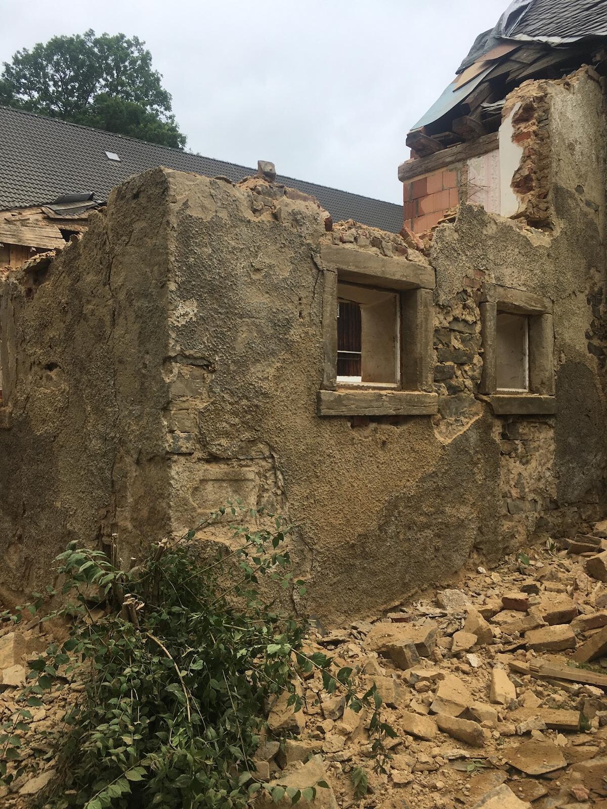 Verlassene Ruine eines verputzten Hauses mit offenen Fenstern, Trümmern und Unkraut.