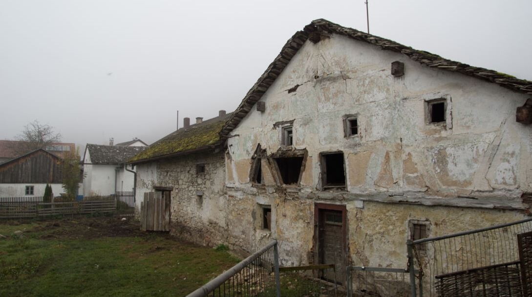 Verfallenes Altbauhaus mit bröckelnder Putzfassade und beschädigten Fenstern