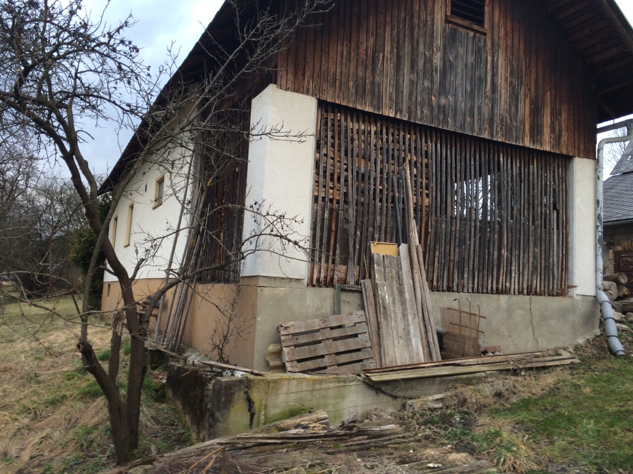 Verfallenes Holzhaus Außenfassade mit Paletten und Baustellenmaterial im Garten.
