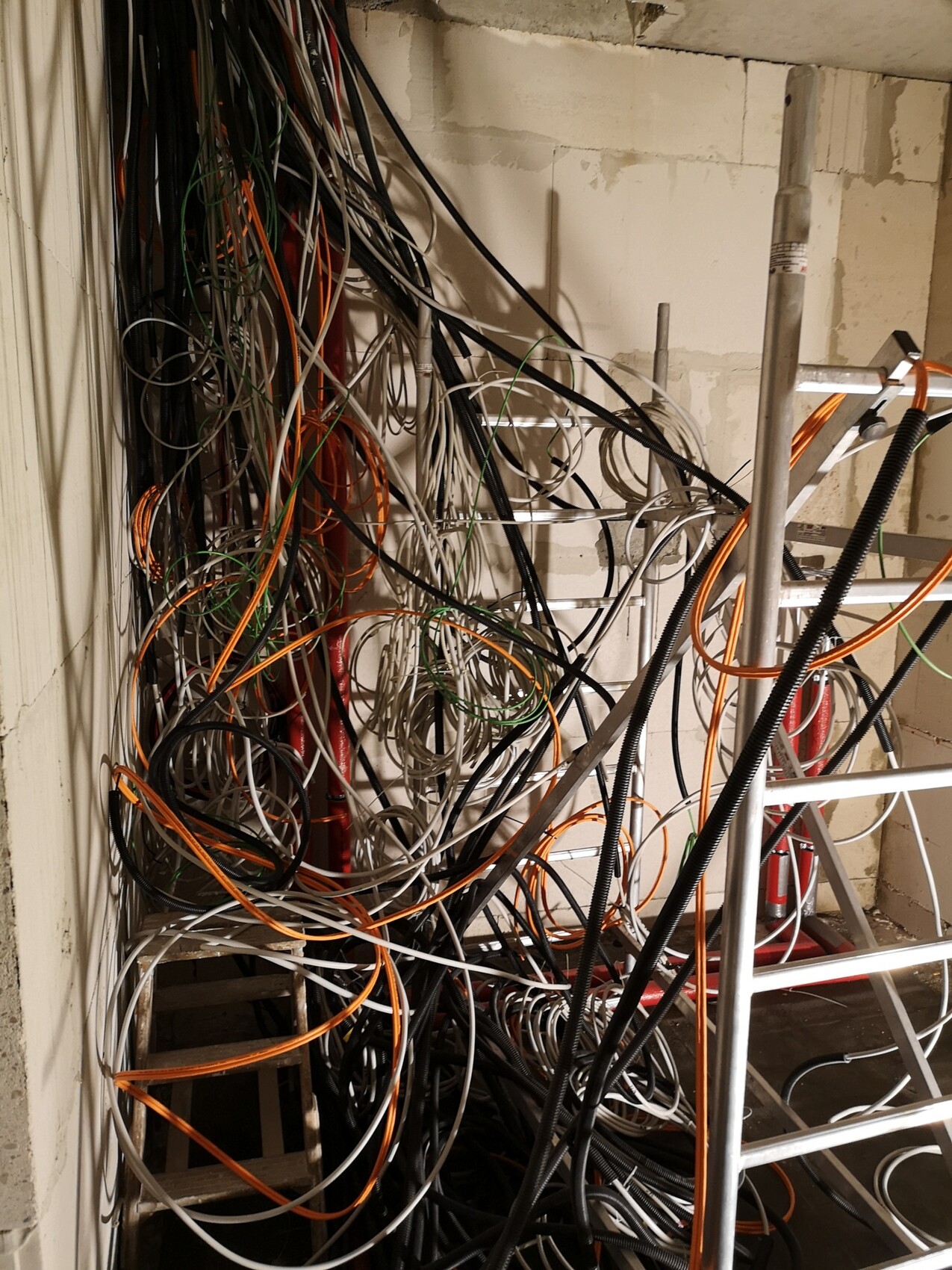 Verhedderte Kabel in Bau-/Technikraum; orange, schwarz und weiß, wirbeln um eine Leiter.