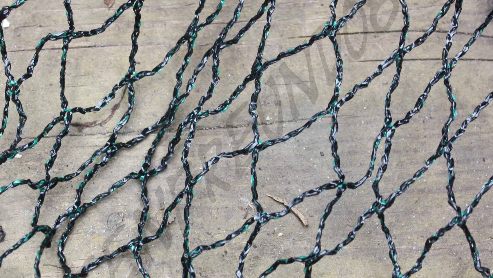 Verheddertes schwarzes und grün gestreiftes Plastiknetz liegt auf Betonboden im Freien.
