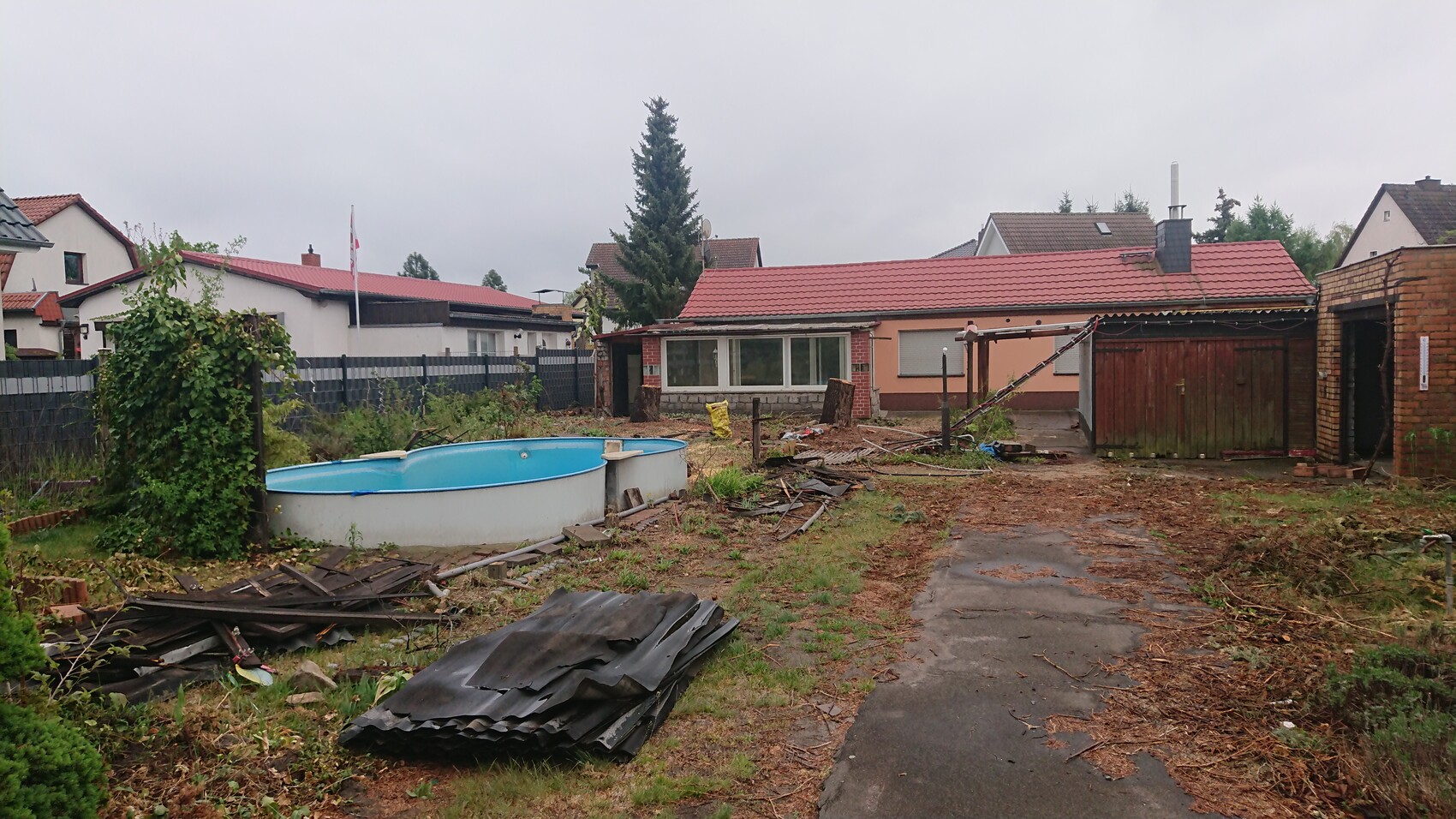 Garten hinter dem Haus mit leerem runden Pool, Bauabfällen und Trümmern.