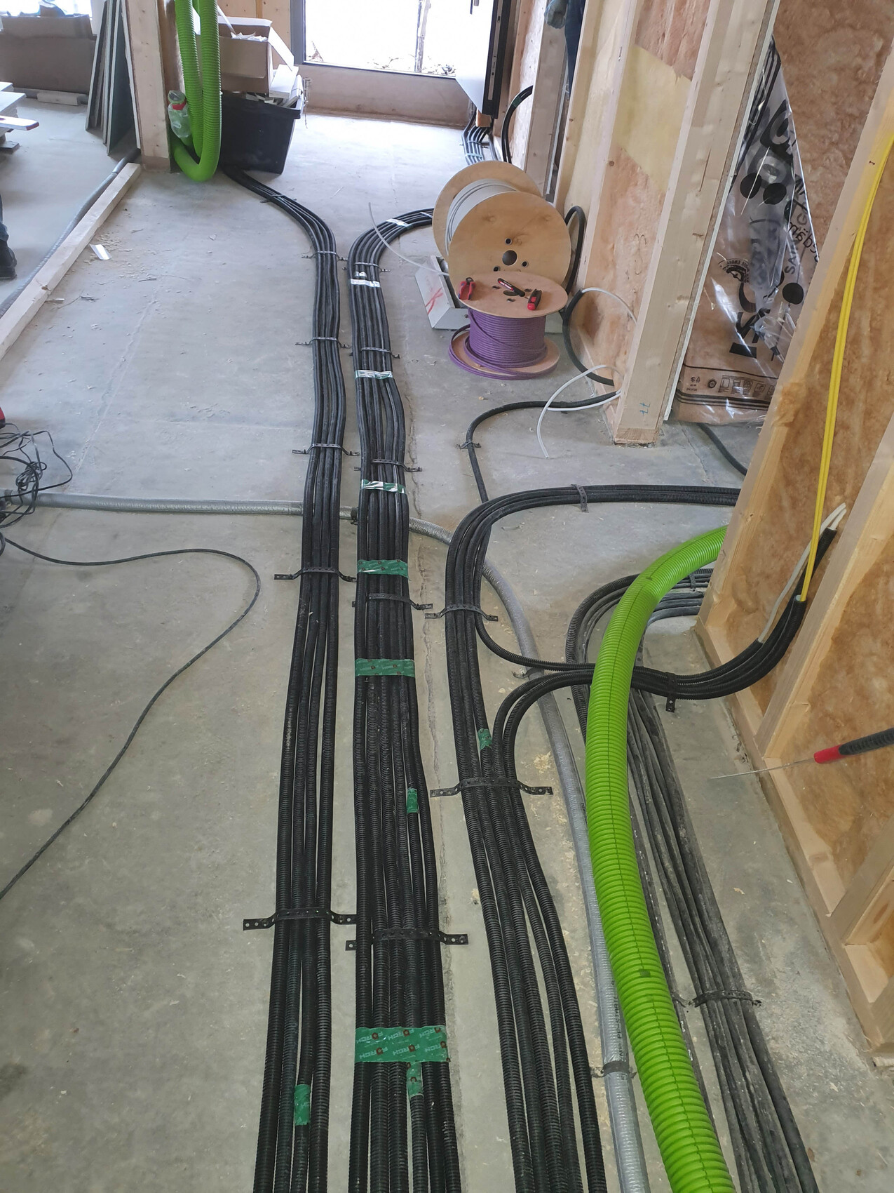 Baustelle: Mehrere schwarze Kabelbündel und grüne Rohre liegen auf dem Boden, Spule mit Kabel.